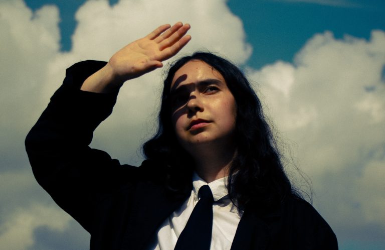 Jana Bahrich of Francis of Delirium shading her eyes against a cloudy blue sky.